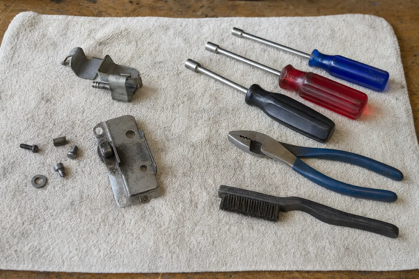 A door latch and strike assembly and a hinge plate with its roller pin, laid out on a towel with nut drivers and pliers